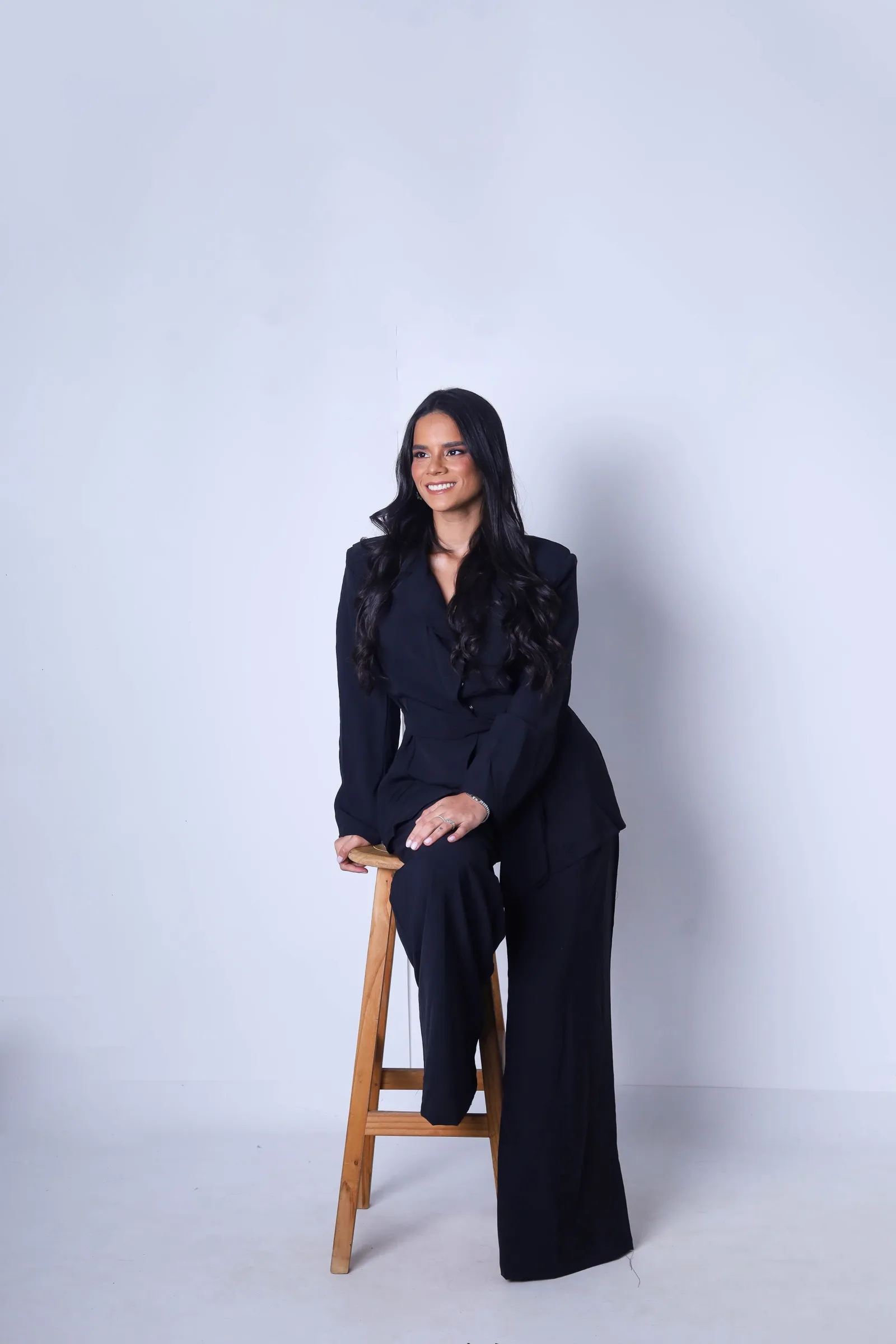 Beatriz Barreto, arquiteta de interiores, sentada em um banquinho de madeira